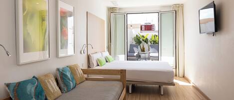 A modern hotel room with a bed, a sofa, a TV, and large windows with a view of the city.