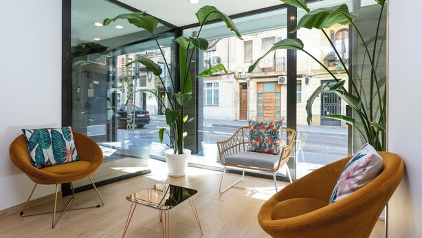 Un interior moderno con dos sillones anaranjados, una mesa de centro de vidrio y ventanas amplias que dan a la calle.