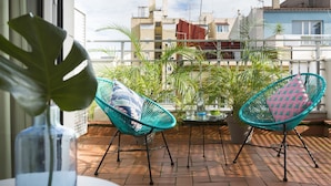 Un balcón con dos sillas turquesas, una planta en maceta y una mesa con un florero de vidrio.
