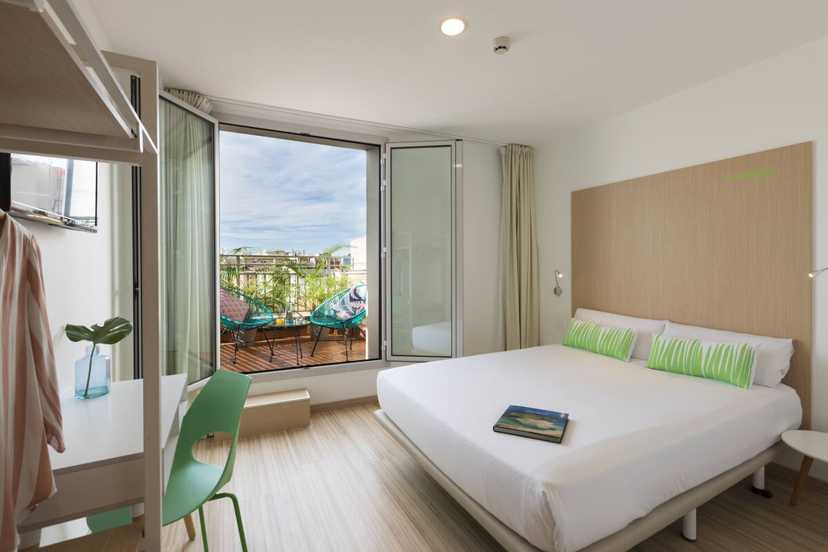 Camera d'albergo con un letto grande, vista sull'esterno, un tavolino e una sedia.