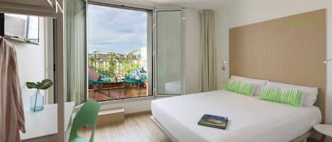 A hotel room with a large bed, a view of the outdoors, a small table, and a chair.
