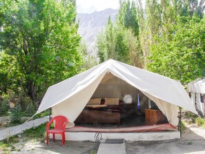 A tent with a sleeping area and a red chair outside, set in a forested area with mountains in the background.