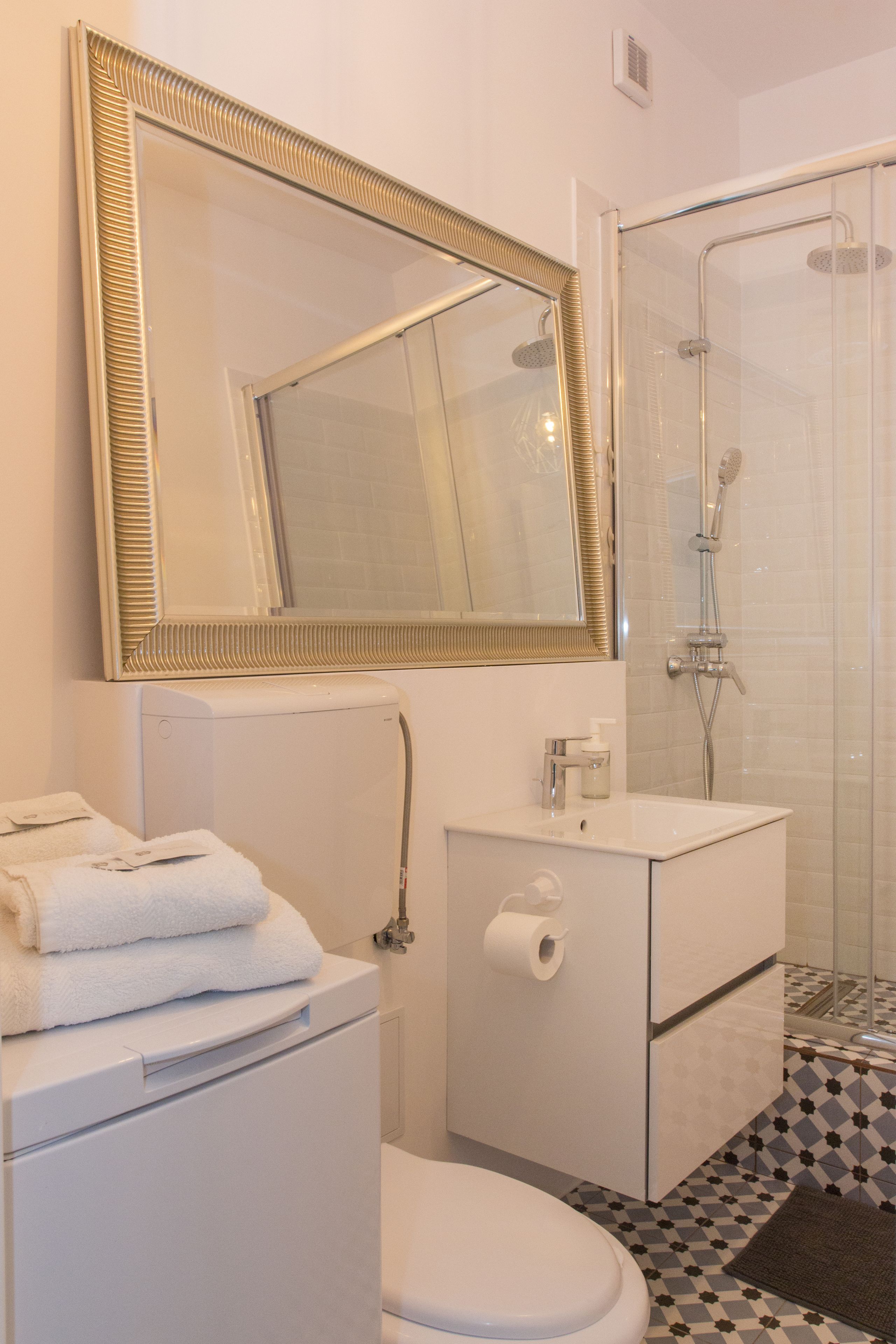 A bathroom with a toilet, sink, mirror, and shower.