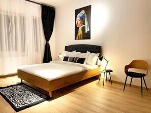 A modern bedroom with a wooden bed, a black and white patterned rug, a wooden chair, and a painting of a woman on the wall. - MRG Apartments (Bucharest)