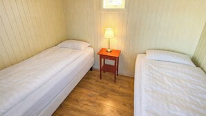 Un alojamiento pequeño, con una sola habitación y dos camas individuales, una mesita de noche de madera con lámpara, y una ventana que deja entrar luz natural.