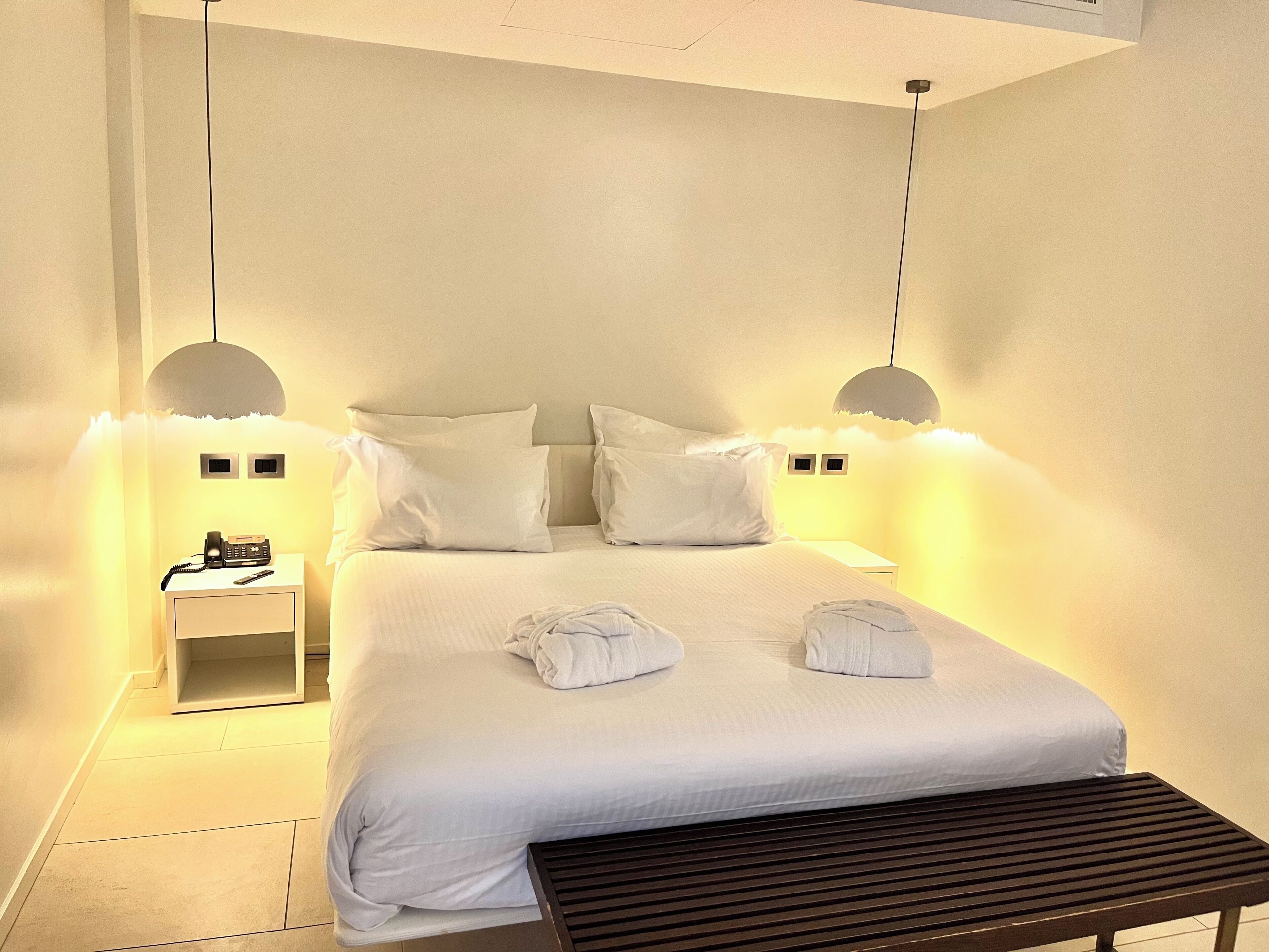 A bedroom with a bed, bedside tables, a telephone, and a bench.
