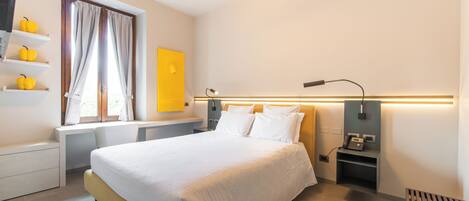 A modern hotel room with a bed, bedside tables, a desk, a lamp, a phone, and a window with curtains.