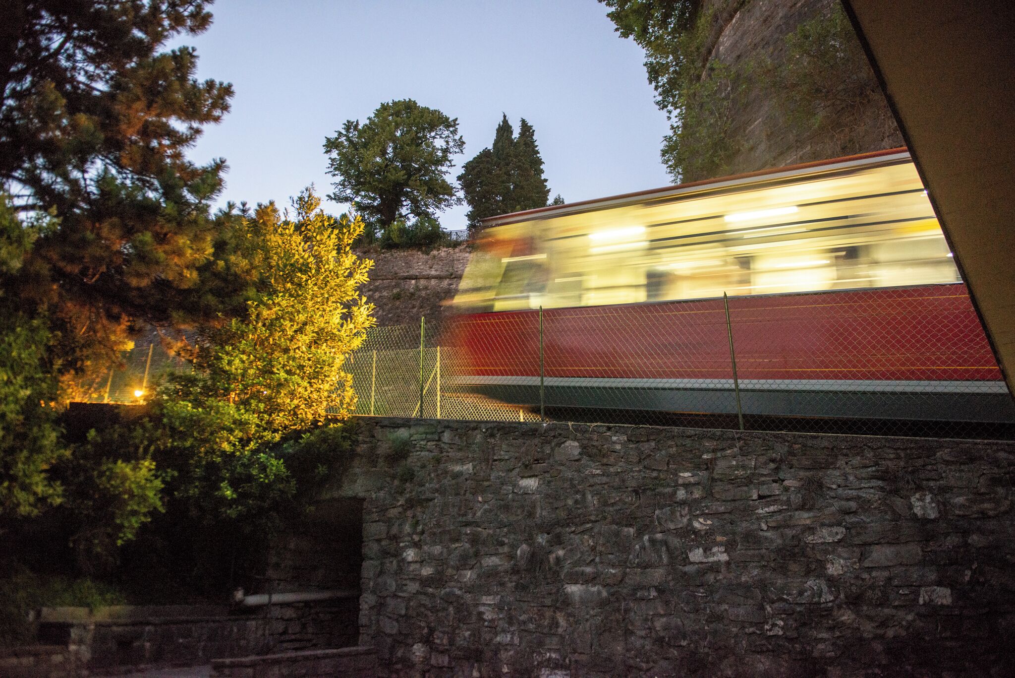 A train passing through a stone wall with a metal fence on one side.