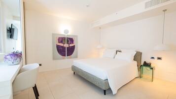 A modern hotel room with a bed, bedside table, lamp, and a painting on the wall.