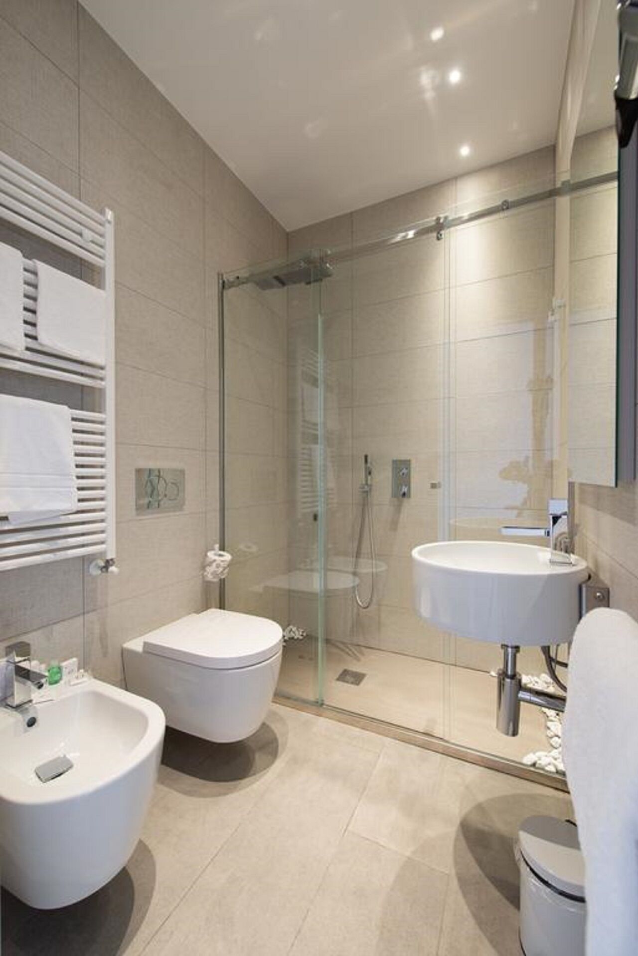 A modern bathroom with a glass-enclosed shower, two white sinks, and a bidet.