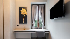 Una habitación moderna con escritorio integrado, una silla, un ventanal con cortinas, televisor montado en la pared y una obra de arte enmarcada.