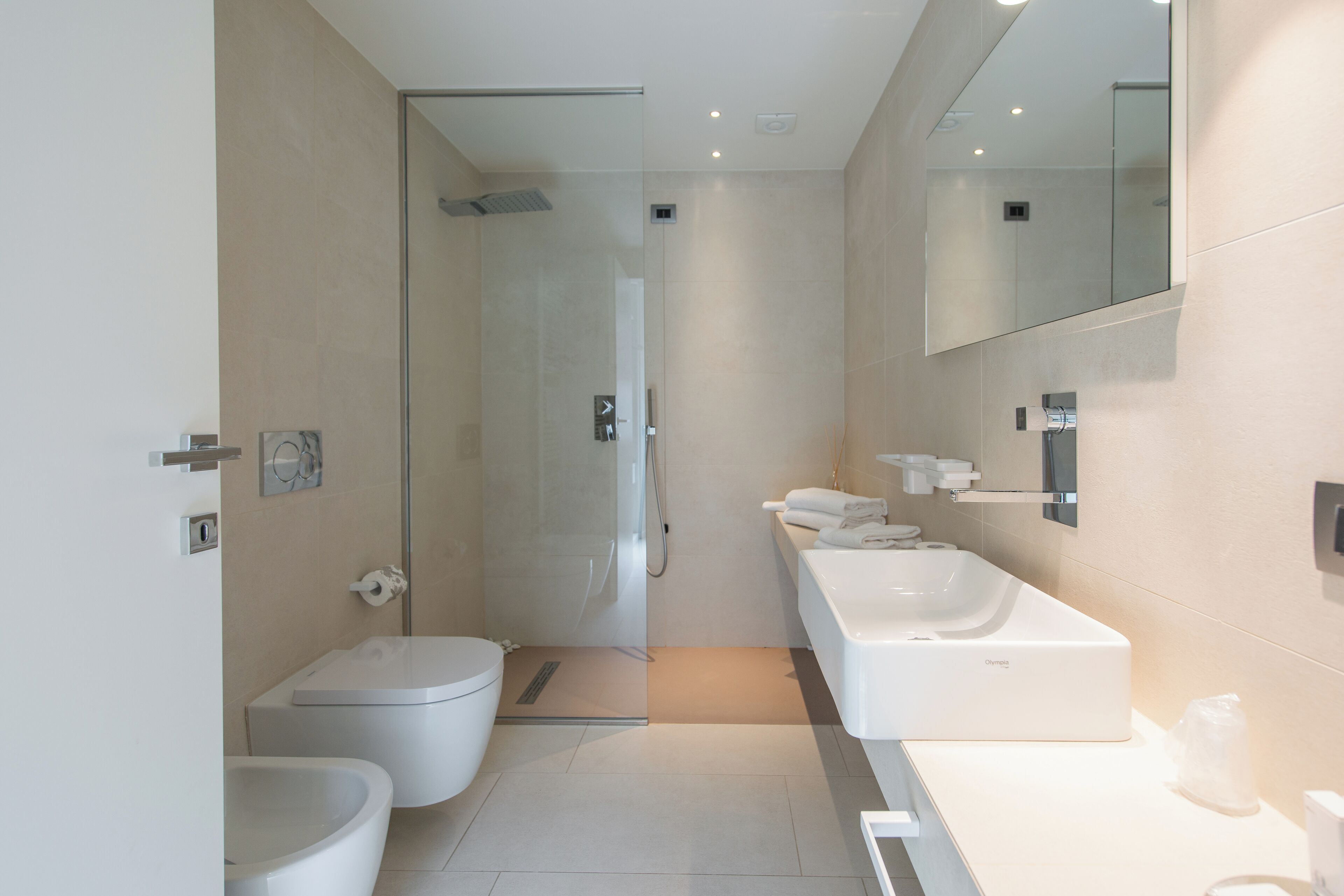 A modern bathroom with a toilet, bidet, shower, and a large mirror.