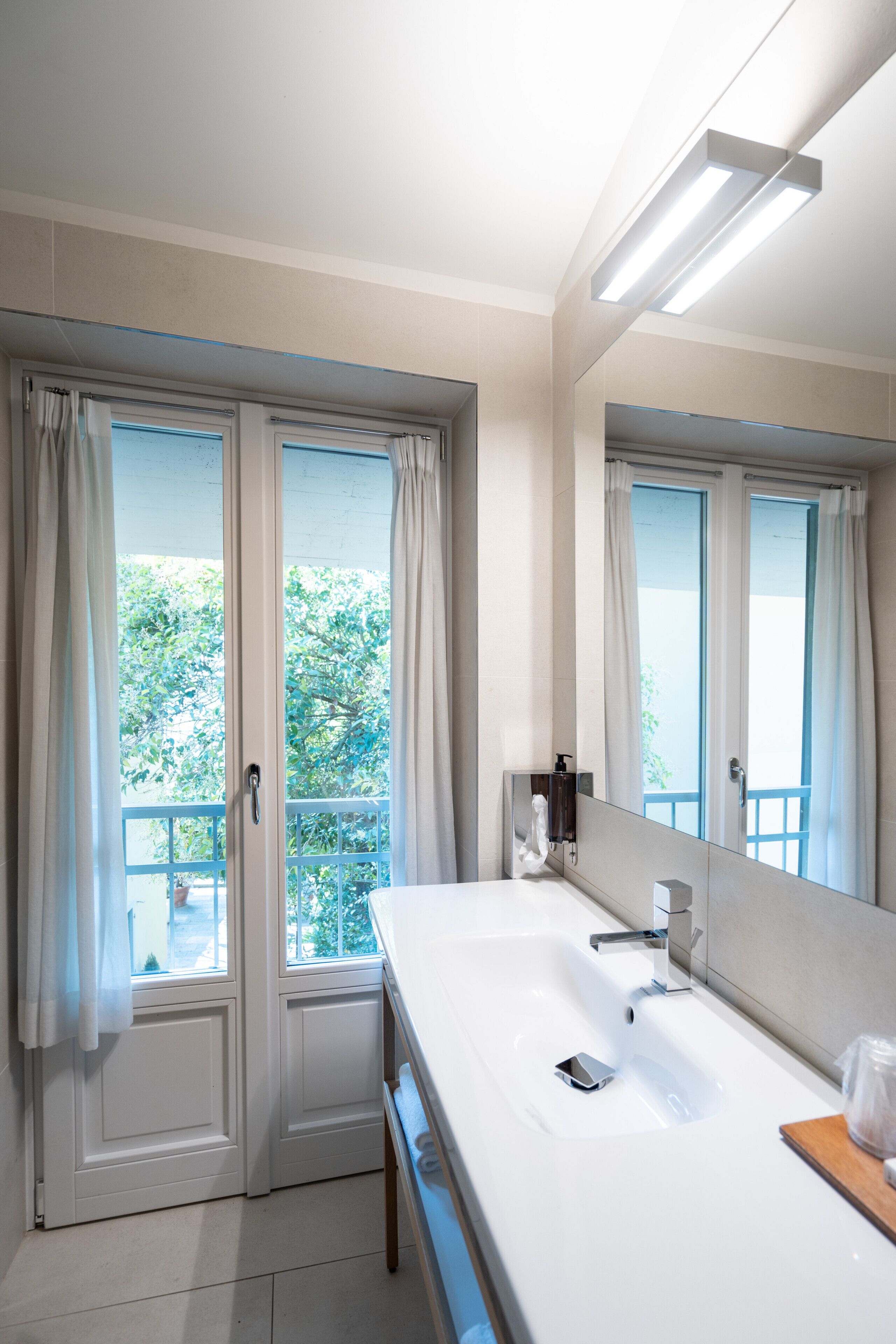 Un bagno con uno specchio grande, un lavandino e una finestra con tende.