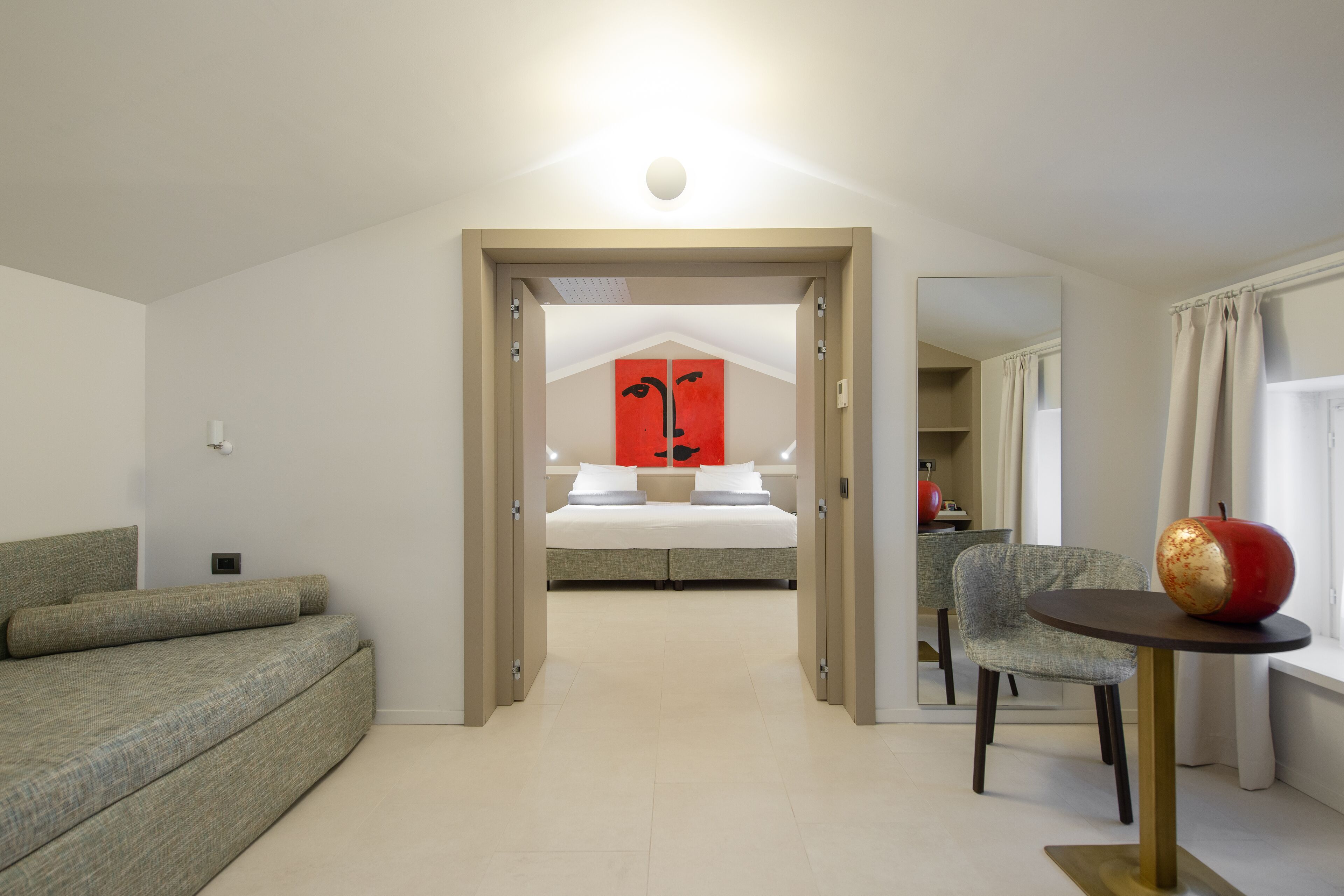 Una habitación de hotel moderna con cama, sofá, mesa de comedor y espejo.
