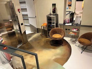 Un interior moderno con suelo curvo, un ascensor de cristal y dos sillones marrones con cojines.