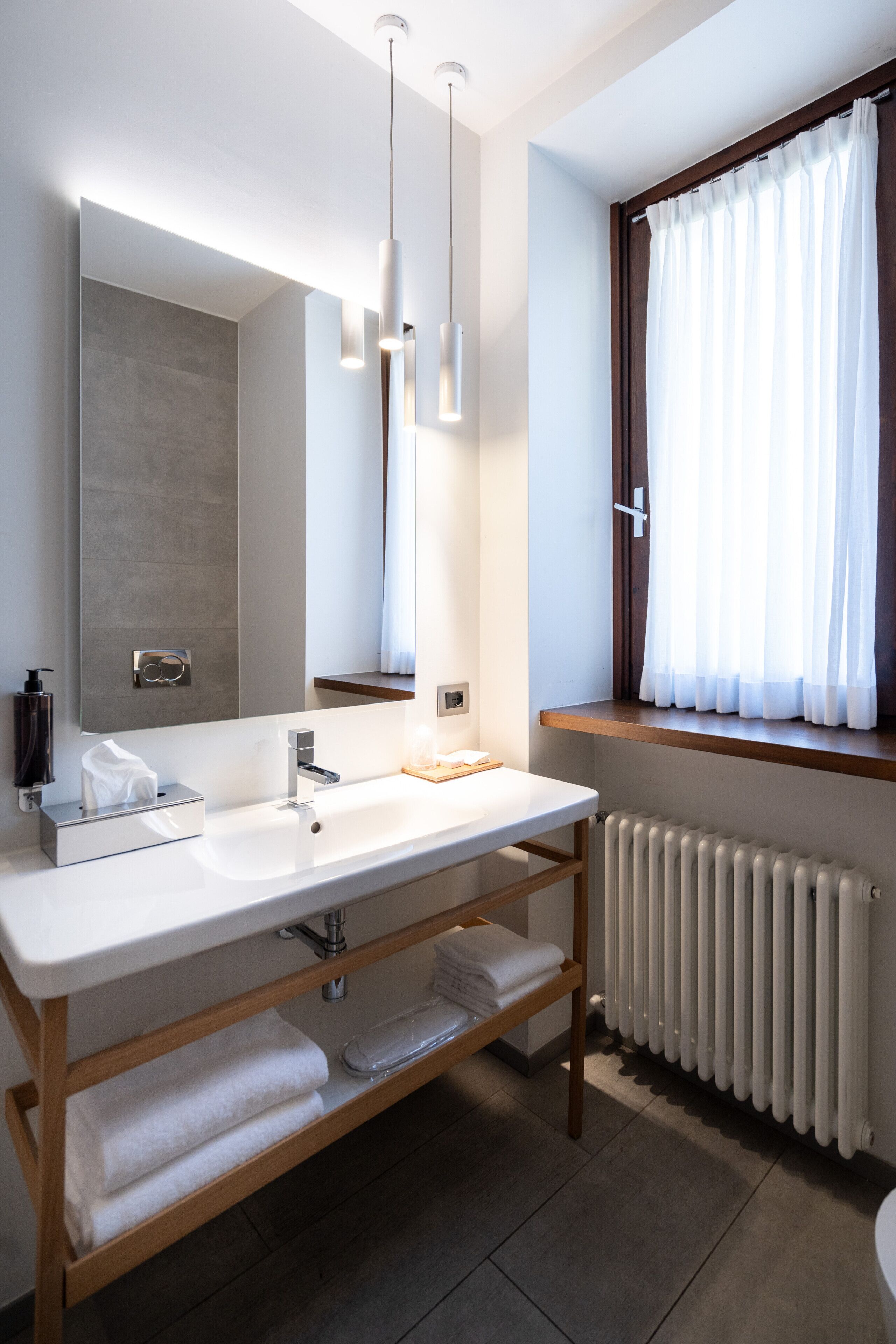 Ein modernes Badezimmer mit einem großen Spiegel, zwei Waschbecken, einem Handtuchhalter und einem fenster mit Vorhängen.