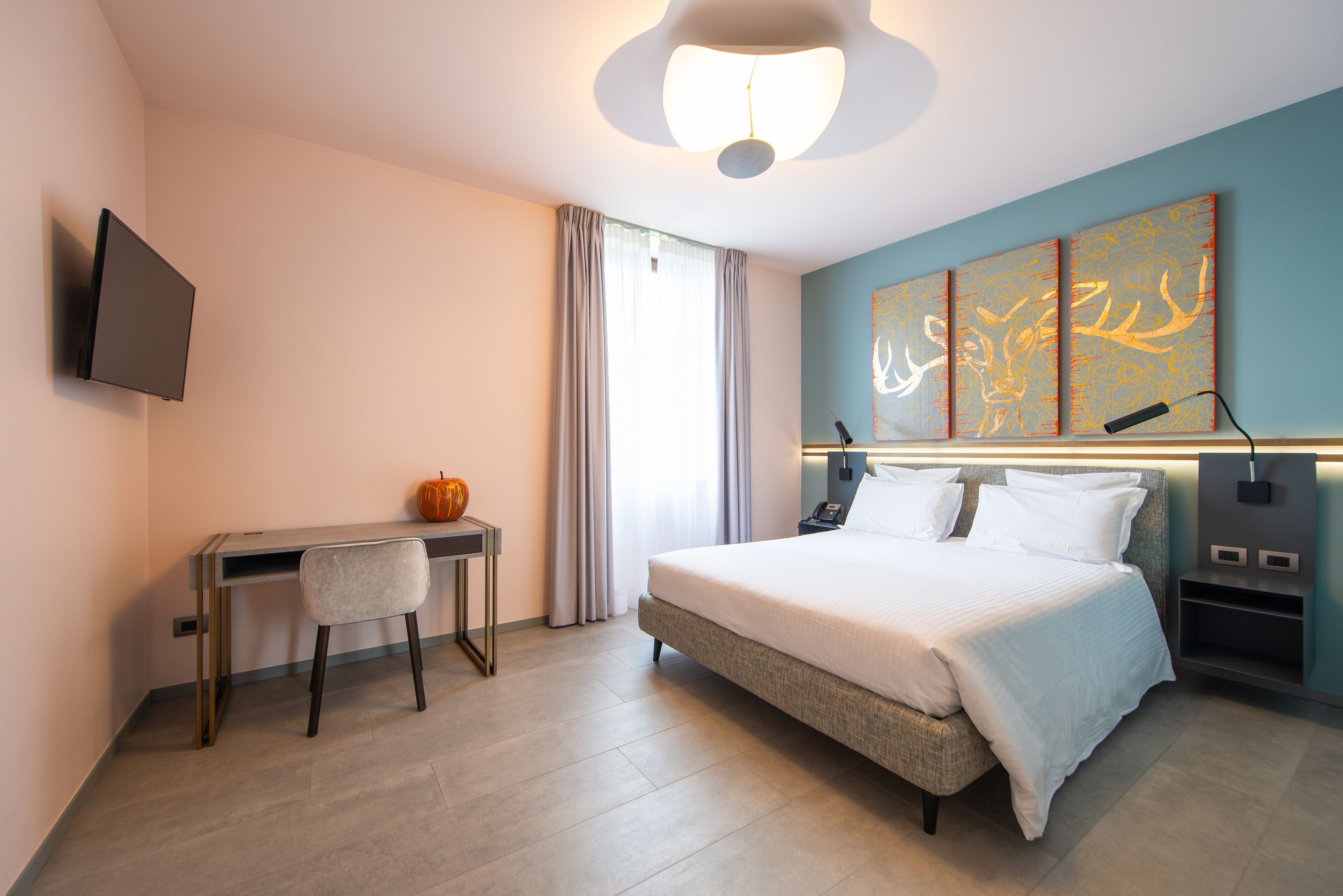 A modern hotel room with a bed, desk, chair, and a flat-screen TV.
