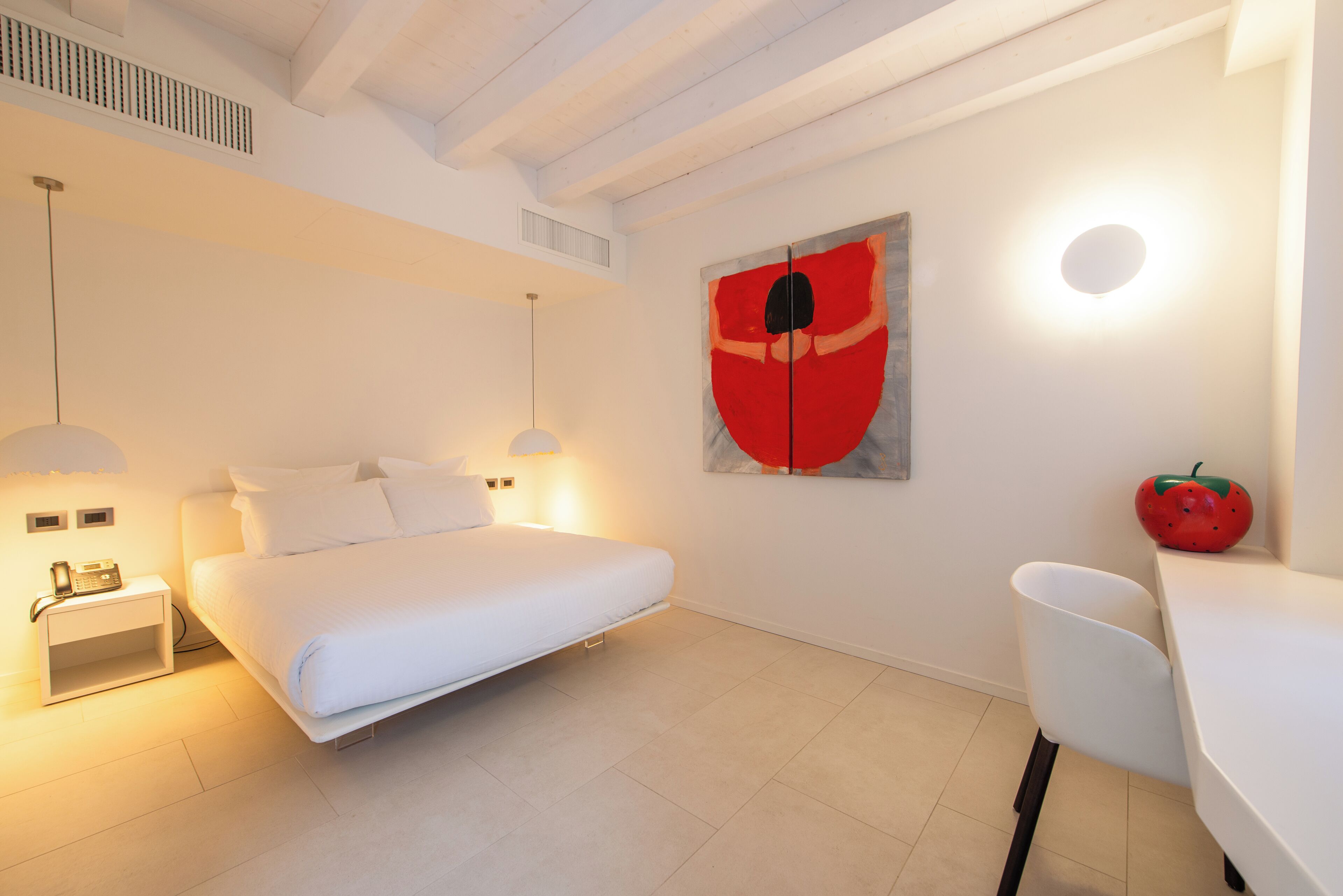 Une chambre à coucher moderne avec un lit, des tables de chevet, une œuvre d’art accrochée au mur et une décoration à base de fruits.