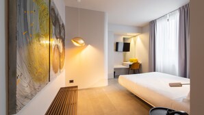 Habitación de hotel moderna con un cuadro abstracto grande, una cama, un escritorio con una silla, un televisor de pantalla plana y un ventanal con cortinas.