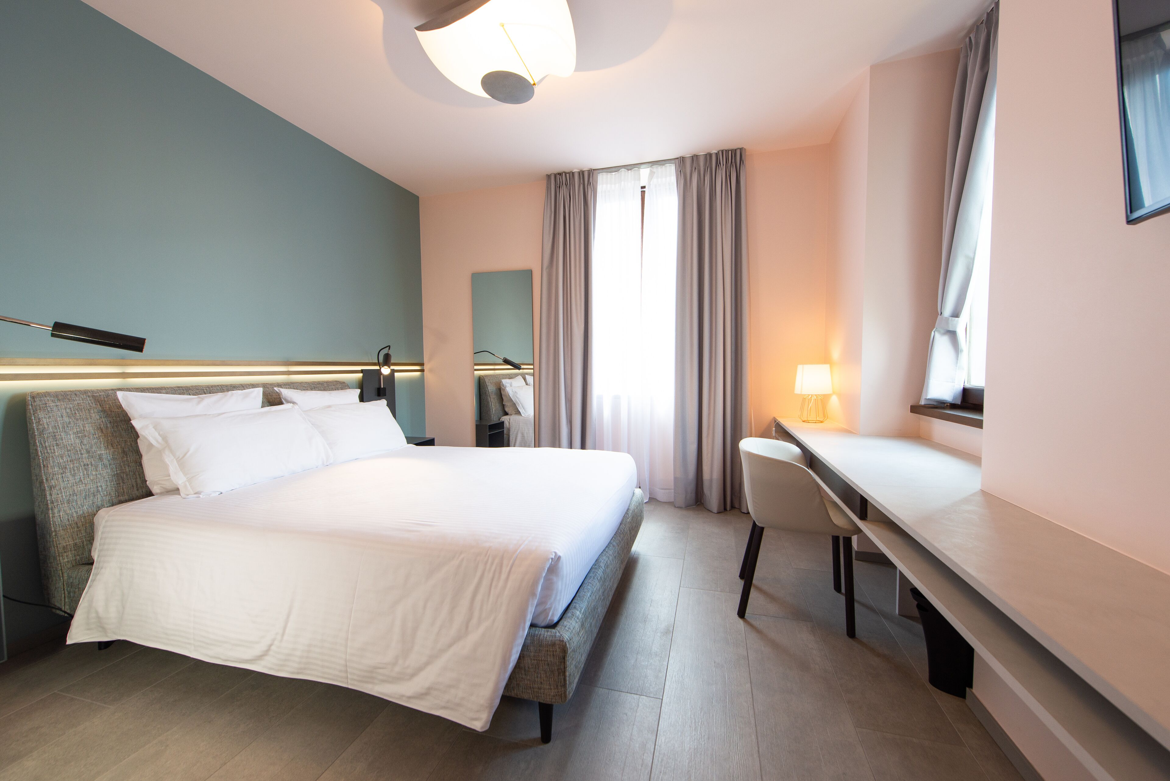 A hotel room with a bed, desk, chair, and a large window with curtains.