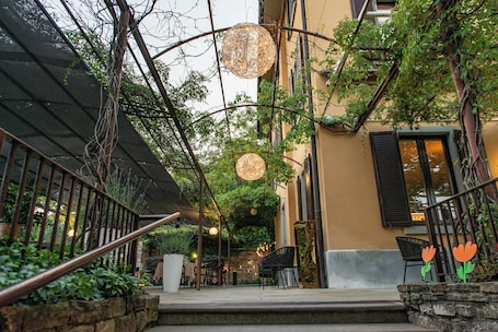 An outdoor seating area with tables and chairs, a stone wall, and a staircase leading to an upper level.. Le Funi Hotel