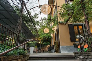 Un'area esterna con tavoli e sedie, un muro in pietra e una scala che conduce a un piano superiore.
