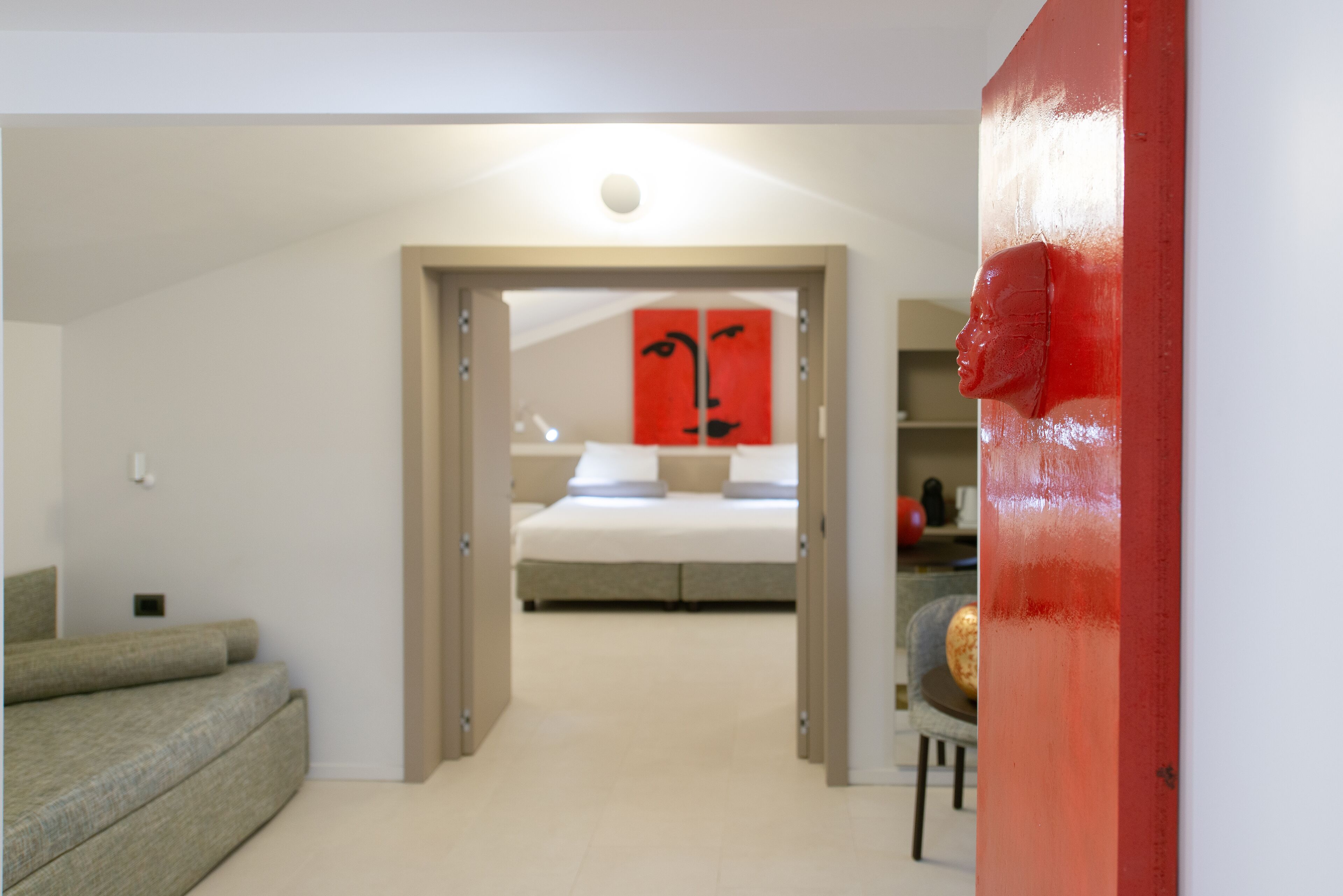 Quarto com cama, parede de destaque vermelha e porta de entrada para outro cômodo.