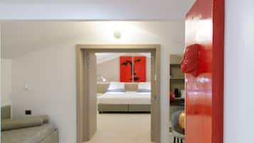 Quarto com cama, parede de destaque vermelha e porta de entrada para outro cômodo.