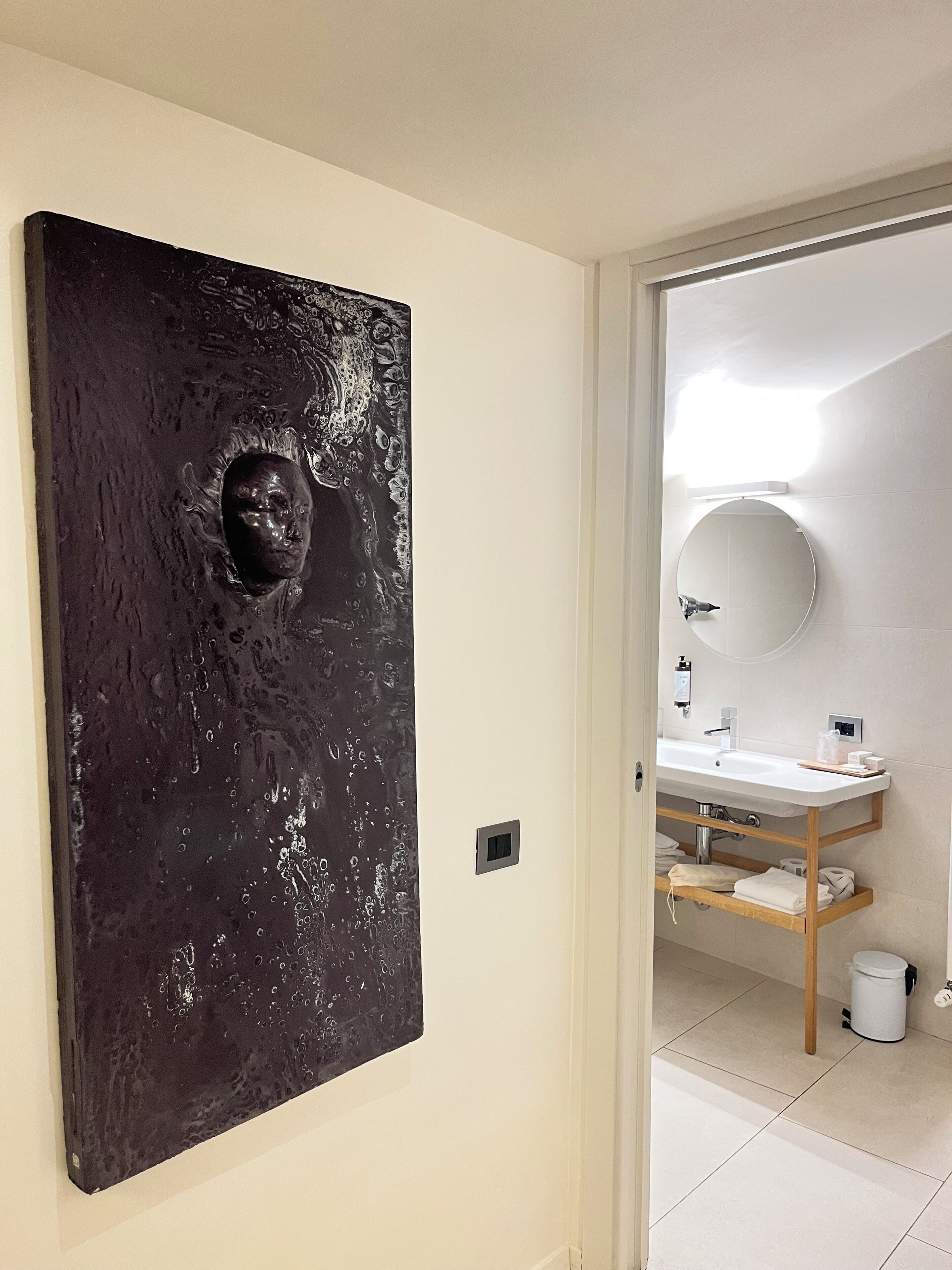 A modern bathroom with a large mirror, a white sink, and a wooden shelf.