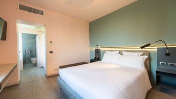 A modern hotel room with a large bed, a bedside table, a nightstand, a wall-mounted lamp, and a view of the bathroom.