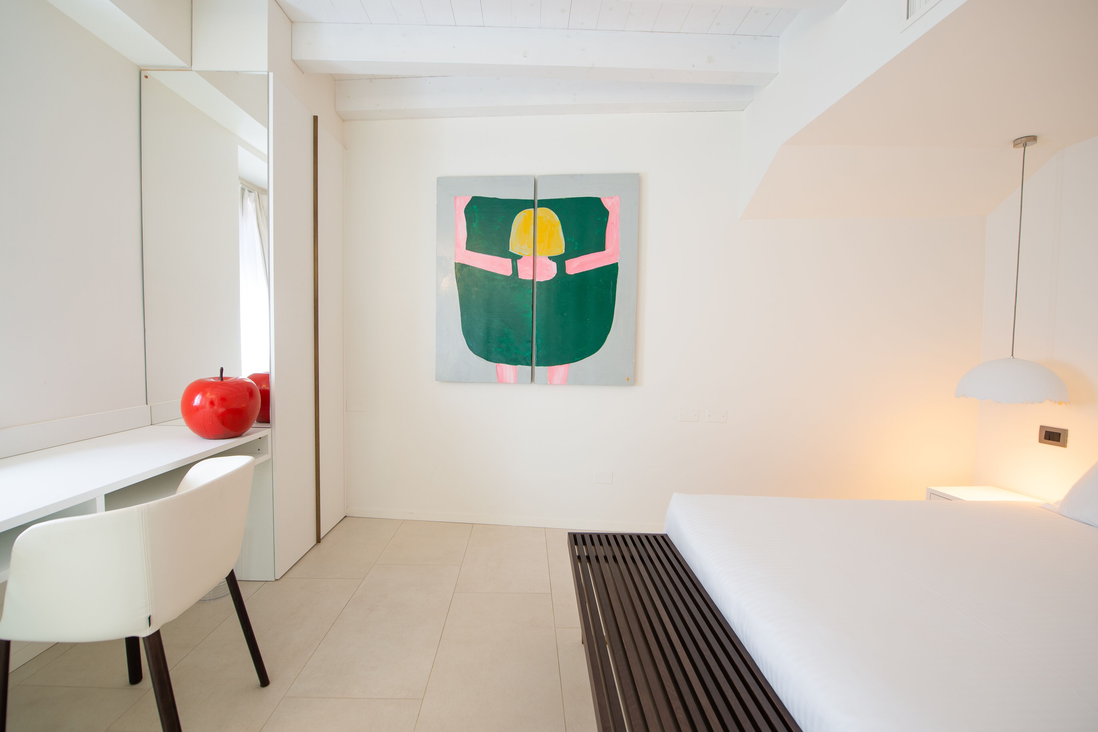 Una habitación de hotel moderna con un escritorio blanco, una cama con cabecero de madera y un cuadro abstracto grande en la pared.