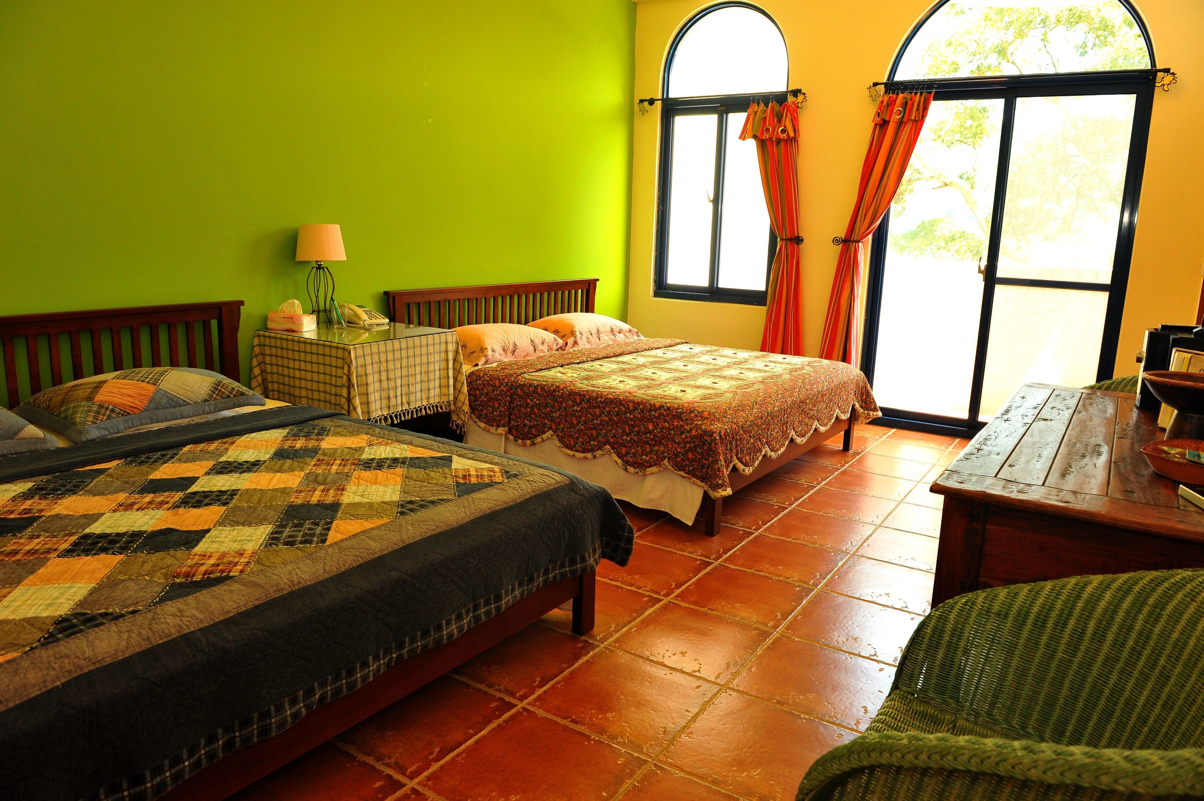 A room with two beds, a small table, a lamp, and a window with curtains.