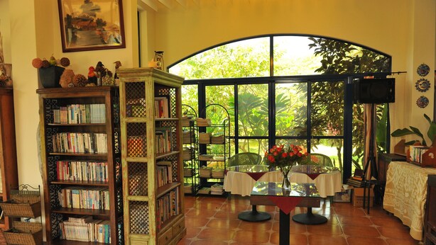 Un rincón acogedor para leer con un ventanal grande, una estantería y una mesa con un jarrón de flores.