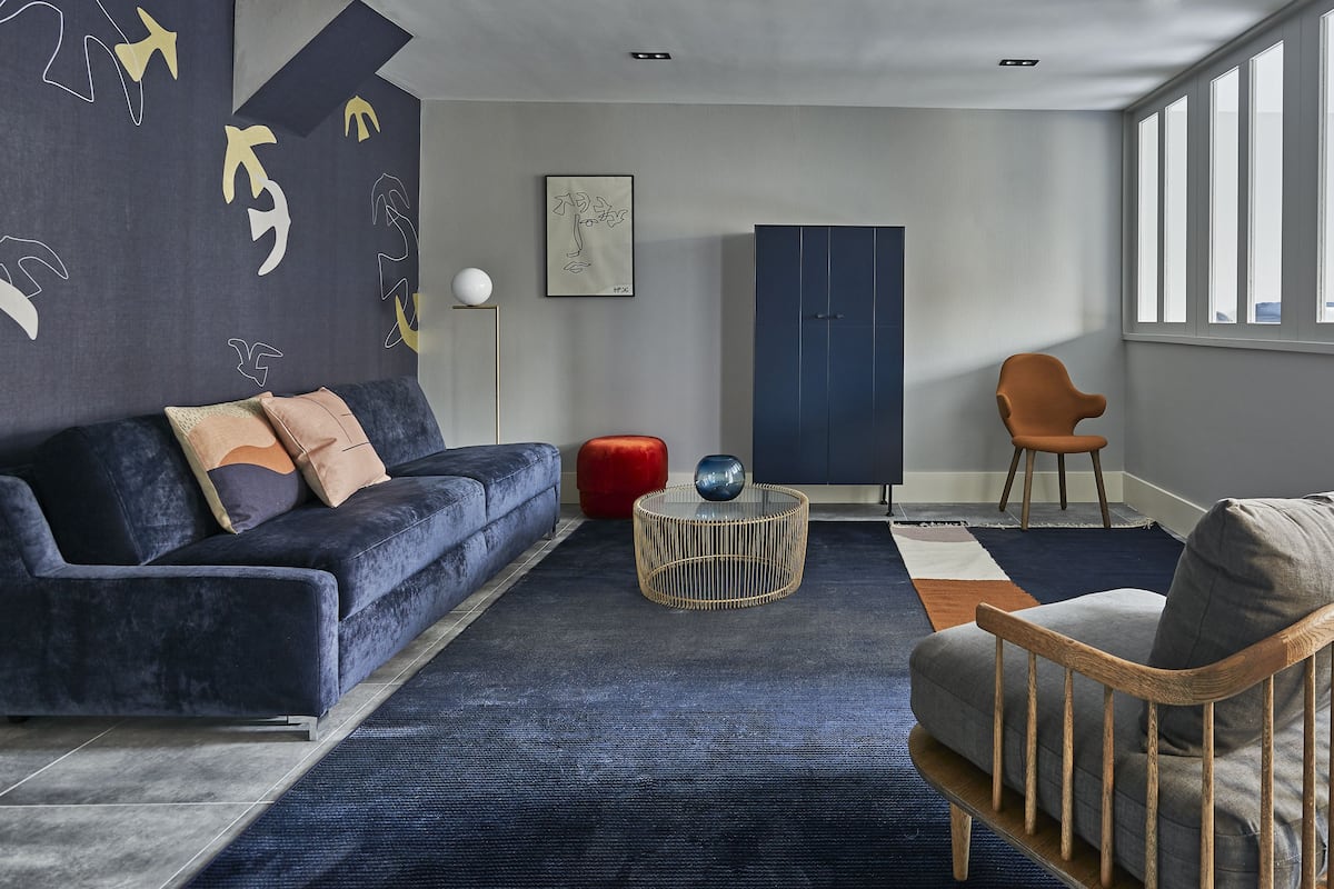 Una moderna camera d'hotel con un divano blu scuro, una sedia in legno, un tavolino rotondo e un'ampia finestra.