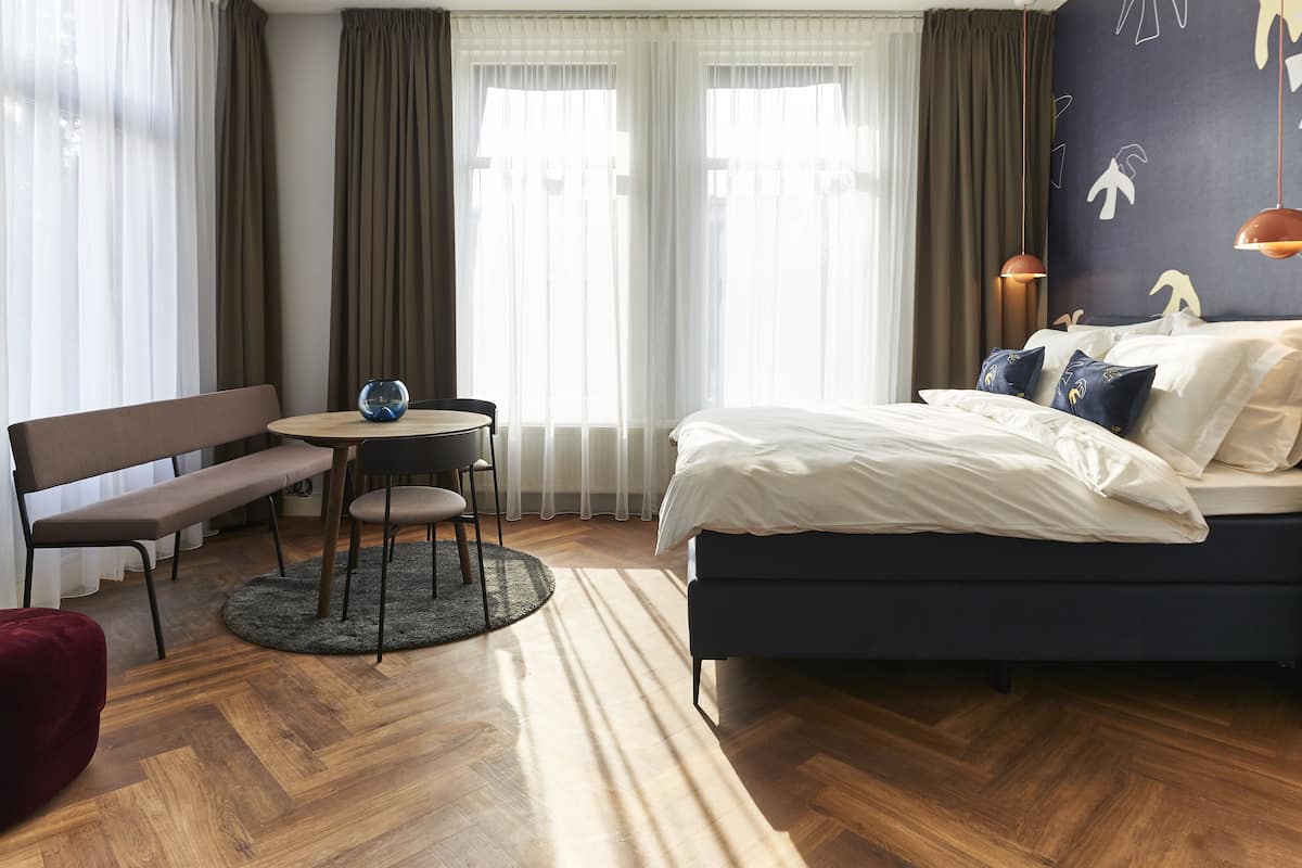 Una camera d'albergo con un letto, una panca, un tavolino e un tappeto rotondo.
