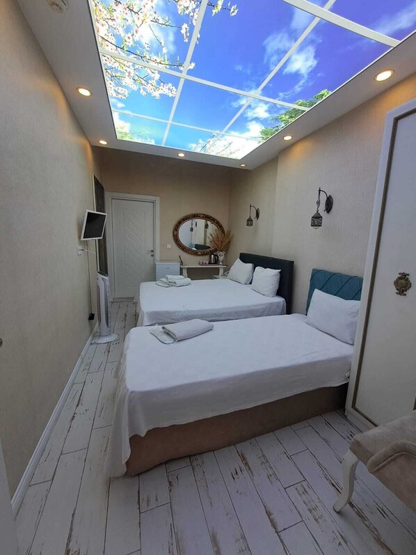 A hotel room with two beds, a skylight, a small table with a mirror, a wall-mounted TV, and a door. - Peri 26 Otel (Eskisehir)