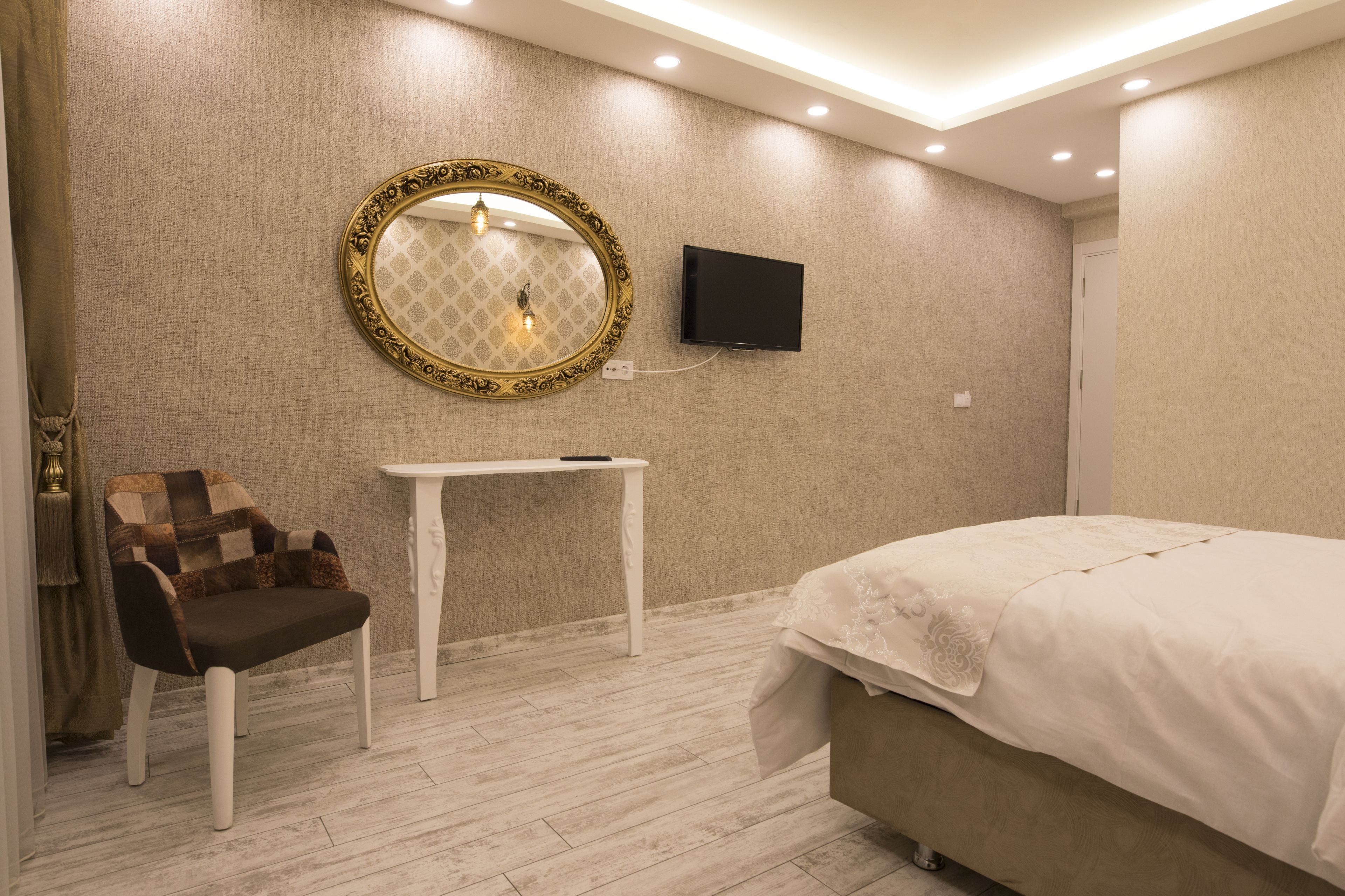 A bedroom with a bed, a TV mounted on the wall, a small table, and a chair.