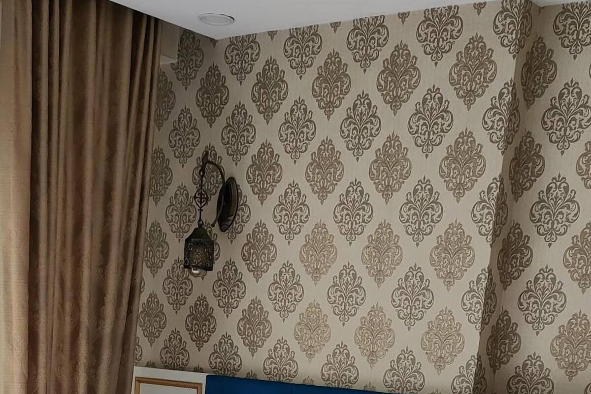 A neatly made bed with white linens, a blue headboard, and a patterned wall.