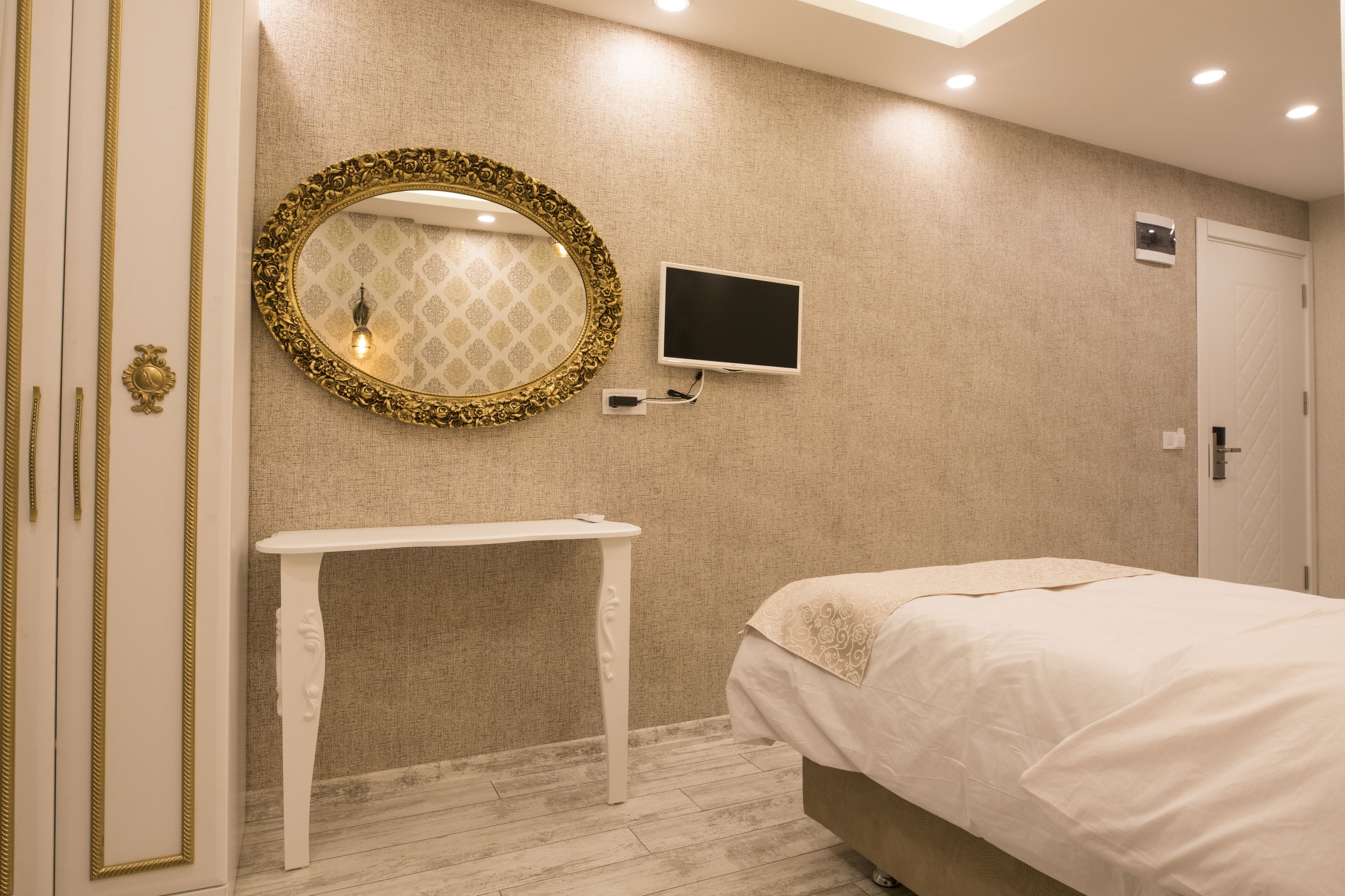 A bedroom with a bed, a vanity with a mirror, a television, and a door.