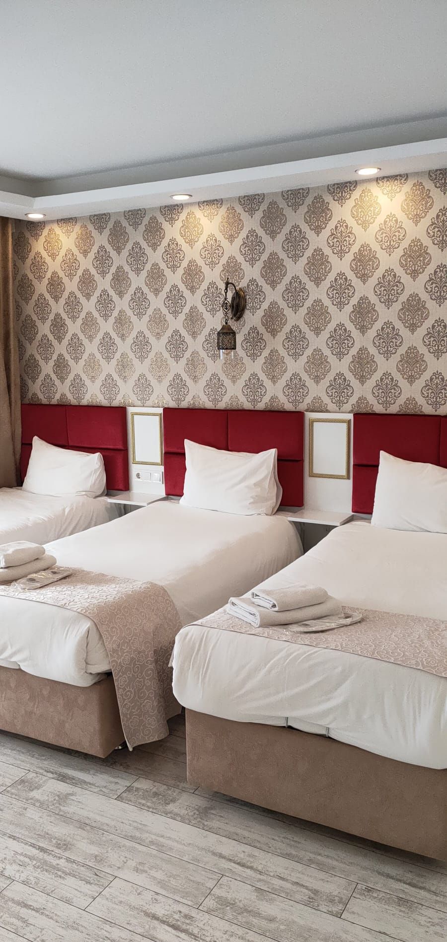 Quarto de hotel com três camas, papel de parede estampado e cabeceira vermelha.