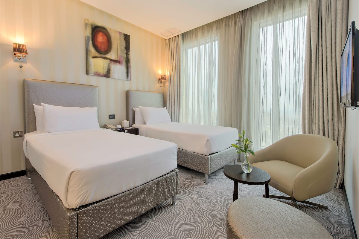 Une chambre d’hôtel avec deux lits, un canapé, une petite table avec un vase et un téléviseur fixé au mur.