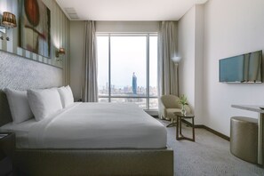 A hotel room with a large bed, a TV, a chair, and a view of a cityscape. - Grand Majestic Hotel (Kuwait City)