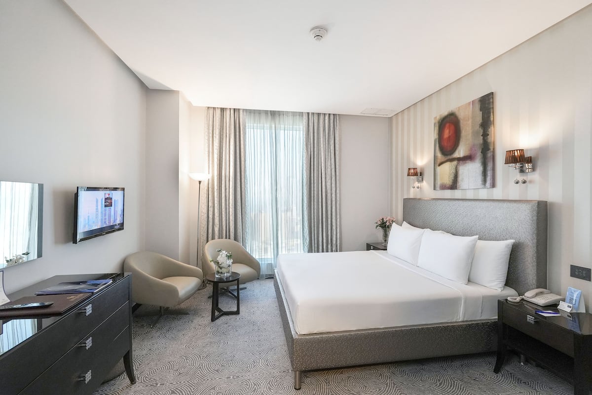 Une chambre d’hôtel avec un grand lit, un bureau avec un ordinateur, une chaise, une petite table avec un vase et un tableau au mur.