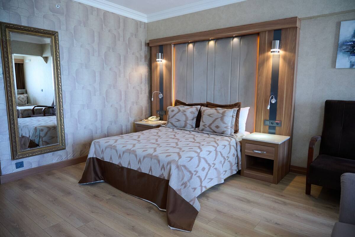 A bedroom with a large bed, wooden headboard, bedside tables, a nightstand, a mirror, and a chair.
