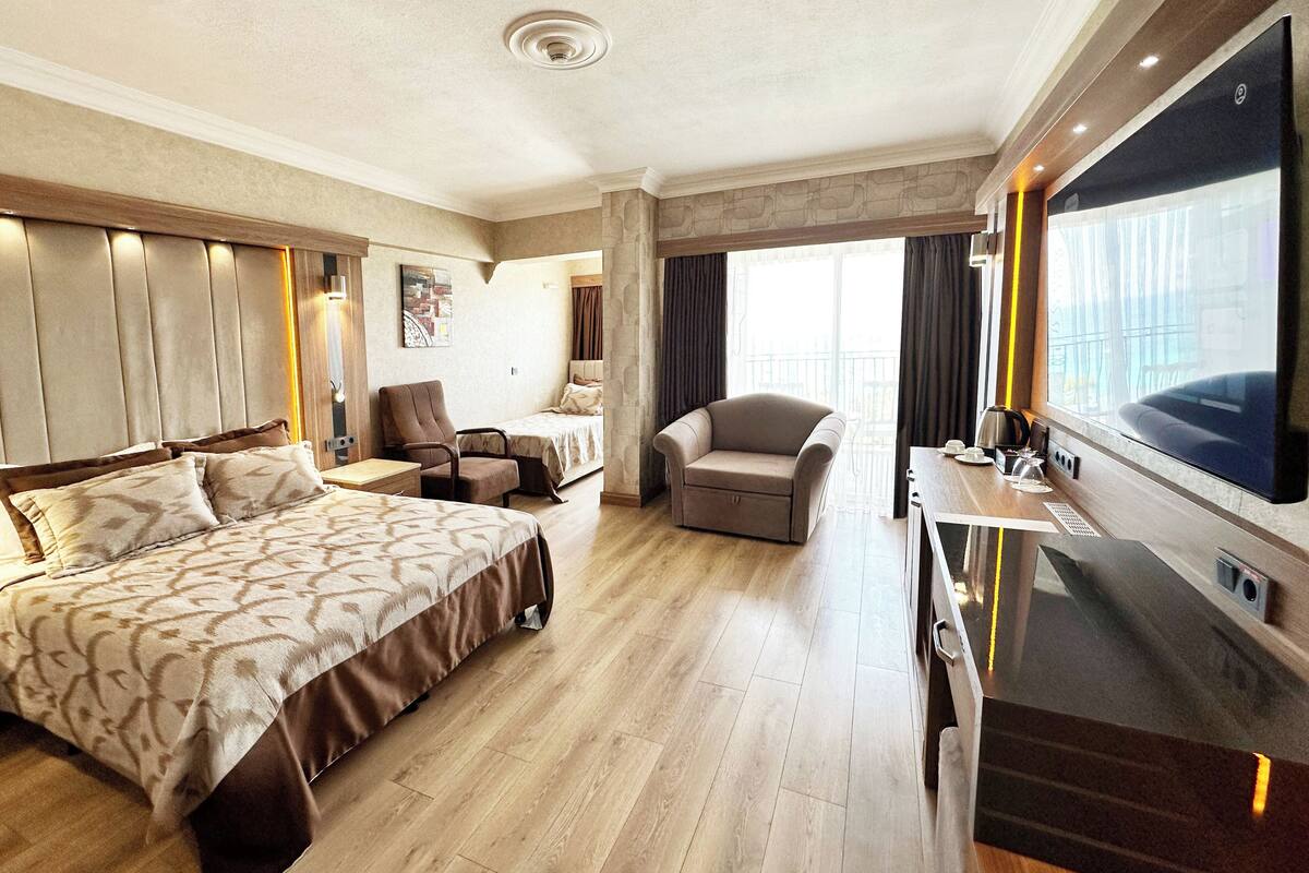 A hotel room with a large bed, a desk with a flat-screen TV, a chair, and a balcony with curtains.