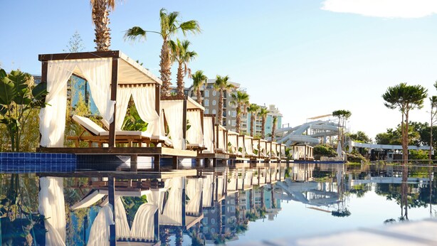 Un hotel lujoso con piscina que refleja la arquitectura, incluyendo una estructura tipo marquesina y palmeras.