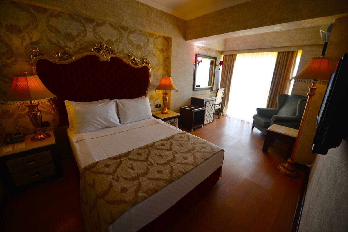 A hotel room with a large bed, two bedside lamps, a chair, a desk, and a television.