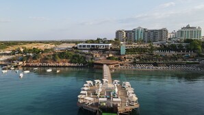 Una plataforma flotante con asientos y sombrillas, amarrada cerca de un puerto deportivo con barcos.