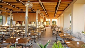 Un restaurante espacioso con mesas y sillas de madera, techo alto con vigas a la vista y lámparas esféricas colgantes.