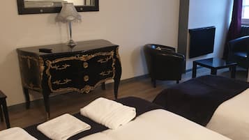A hotel room with a large bed, a small desk with a lamp, a chair, a radiator, and a window with curtains.